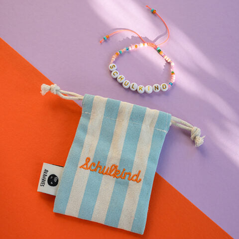 Perlenarmband Schulkind in orange/rosa und goldenen Buchstaben mit Säckchen in hellblau/weiss